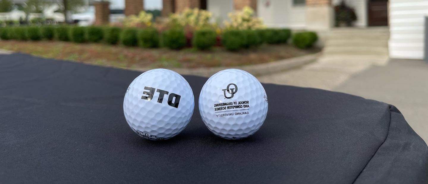 Two golf balls sitting on a table, one with a DTE logo and one with an OU logo